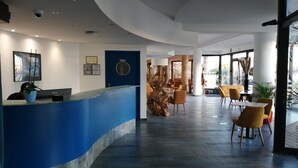 A modern reception area with a blue counter, a reception desk, and a seating area with yellow chairs and tables.