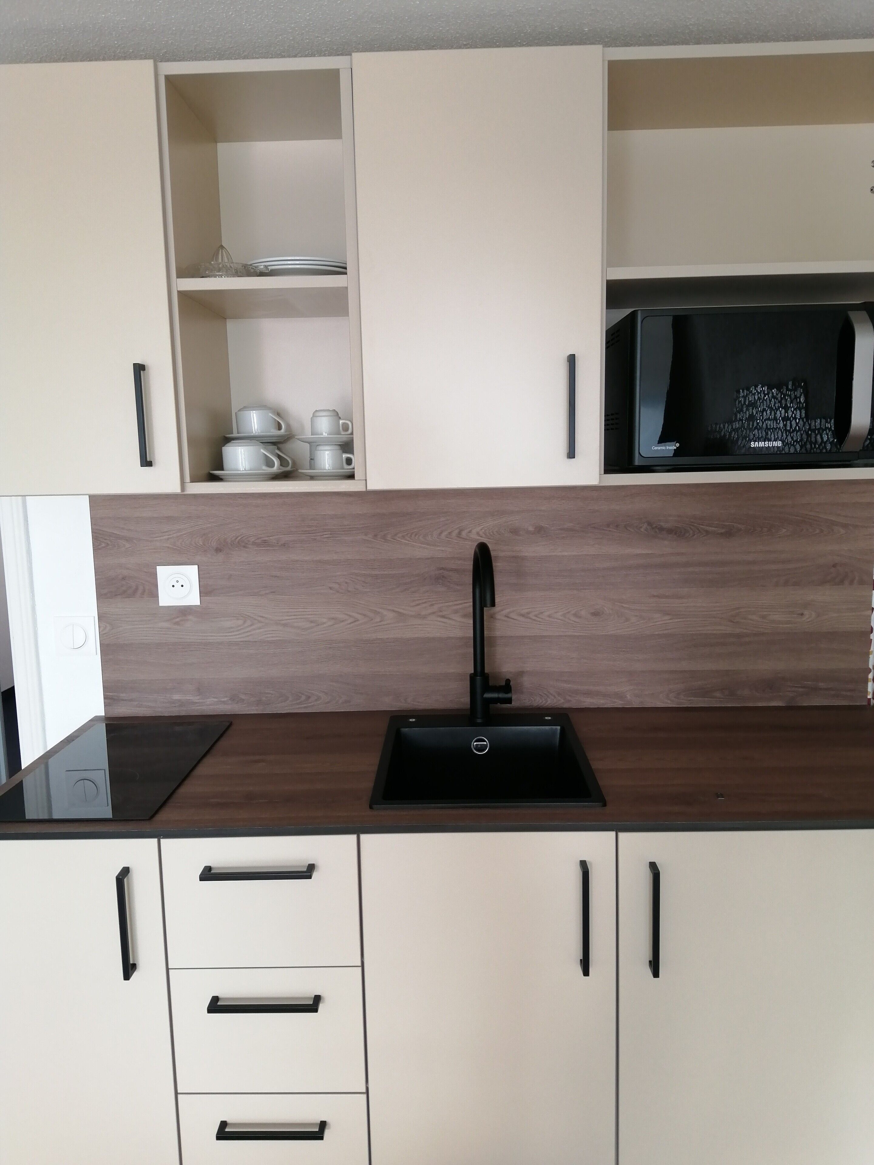 A modern kitchen with a black sink, wooden backsplash, and white cabinets.