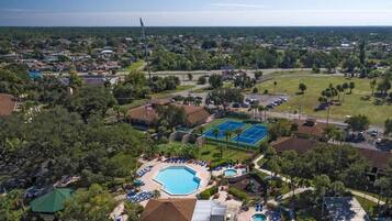 An aerial view of a residential area with a large swimming pool, tennis courts, and a park.