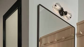 Un bagno moderno con una porta a cornice nera, un grande specchio, uno scaffale in vetro con articoli da toilette e un porta asciugamani in metallo nero.