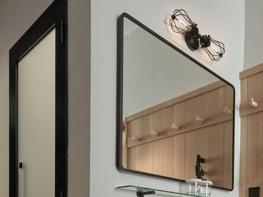 Un bagno moderno con una porta a cornice nera, un grande specchio, uno scaffale in vetro con articoli da toilette e un porta asciugamani in metallo nero.