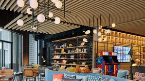 A modern lounge area with a blue sofa, leather chairs, and a bookshelf filled with books and toys. - Moxy Kuala Lumpur Chinatown (Kuala Lumpur)