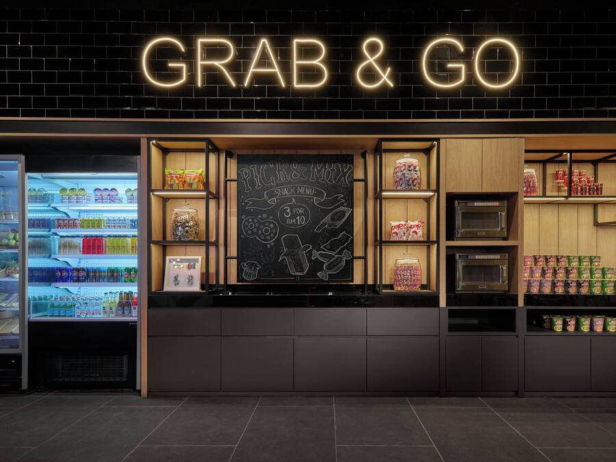 En 'GRAB & GO' kiosk med en neonskilte, en tavlemenu og hylder fyldt med snacks og drikkevarer.