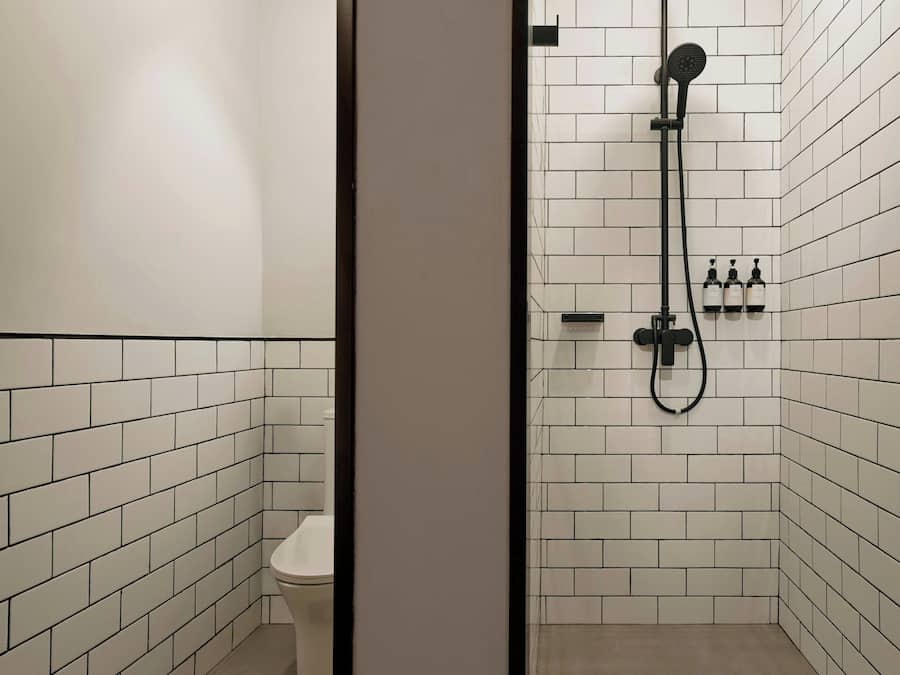 Un baño con paredes de azulejos blancos, un inodoro y una zona de ducha con cabezal de ducha manual.