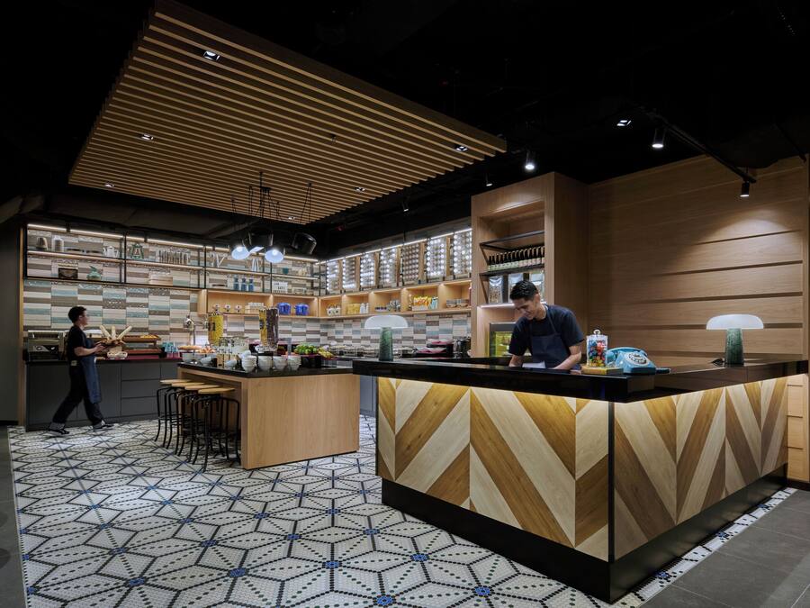 A modern restaurant interior with a central wooden counter, bar stools, and a patterned floor.