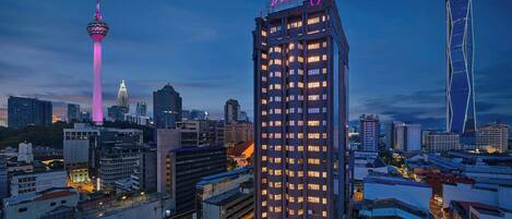 A high-rise hotel with a neon sign, surrounded by other buildings and a prominent tower in the background.