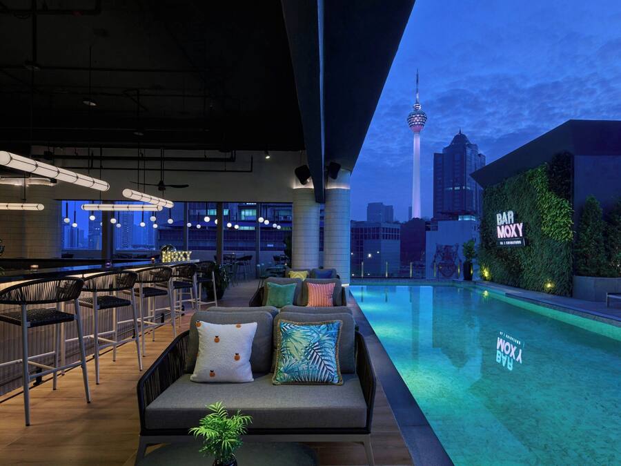 A rooftop bar with a pool, seating, and a city skyline view.