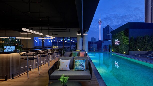 A rooftop bar with a pool, lounge chairs, and a view of the city skyline including a tower. - Moxy Kuala Lumpur Chinatown (Kuala Lumpur)