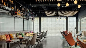 Un interior moderno con una larga mesa de comedor, asientos acolchados y una pared decorativa con patrones geométricos.