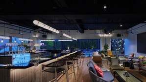 A modern bar area with a bar counter, stools, and a seating area with couches and chairs. - Moxy Kuala Lumpur Chinatown (Kuala Lumpur)