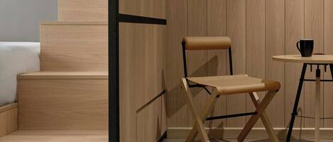A compact room with a wooden staircase, a foldable table, a chair, and a small table with a cup.
