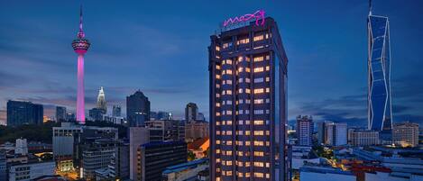 A high-rise hotel with a prominent neon sign, surrounded by other buildings and a tower with pink lighting.