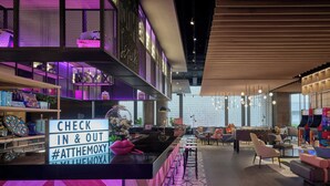 A modern bar area with a check-in/out sign, bar stools, and a dartboard. - Moxy Kuala Lumpur Chinatown (Kuala Lumpur)