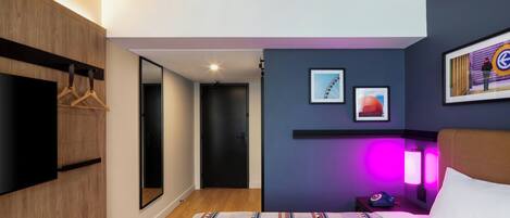 A modern hotel room with a bed, a TV, a wardrobe, and a mirror.