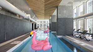 An indoor swimming pool with wooden ceiling beams, lounge chairs, and a pink flamingo float. - New Hotel Moxy Montreal Downtown (Montreal)