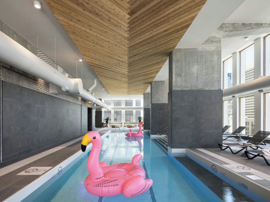 Una piscina interior con vigas de madera en el techo, sillas de descanso y un flotador con forma de flamenco rosa.