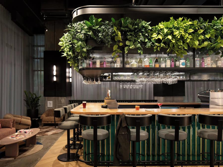 Zona de bar con mostrador de madera, taburetes y una variedad de botellas y vasos.