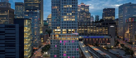 Een modern hotel met een opvallende glazen gevel, een dakterras en een treinstation in de buurt.