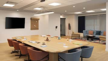 A conference room with a large table, multiple chairs, a flat-screen TV, and a sofa in the background.