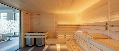 Un sauna avec des bancs en bois et une table chauffante centrale, une porte en verre donnant sur l’extérieur et un sol carrelé.