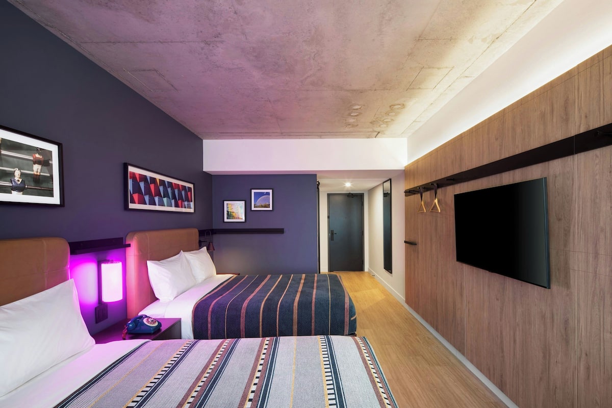 Quarto de hotel moderno com uma cama grande, uma TV e um painel de parede em madeira.