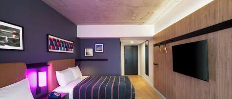 A modern hotel room with a large bed, a TV, and a wooden accent wall.