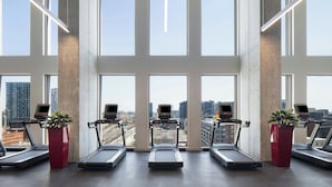 A gym with treadmills, exercise bikes, and large windows offering a city view. - New Hotel Moxy Montreal Downtown (Montreal)