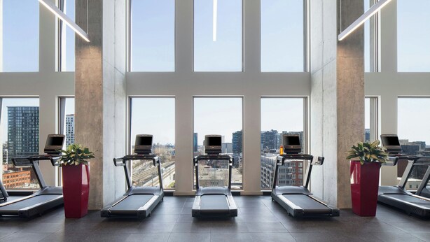 A gym with treadmills, exercise bikes, and large windows offering a city view. - New Hotel Moxy Montreal Downtown (Montreal)