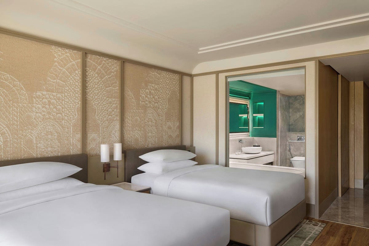 Une chambre d’hôtel avec deux lits, un grand miroir et une salle de bain visible à travers une porte ouverte.