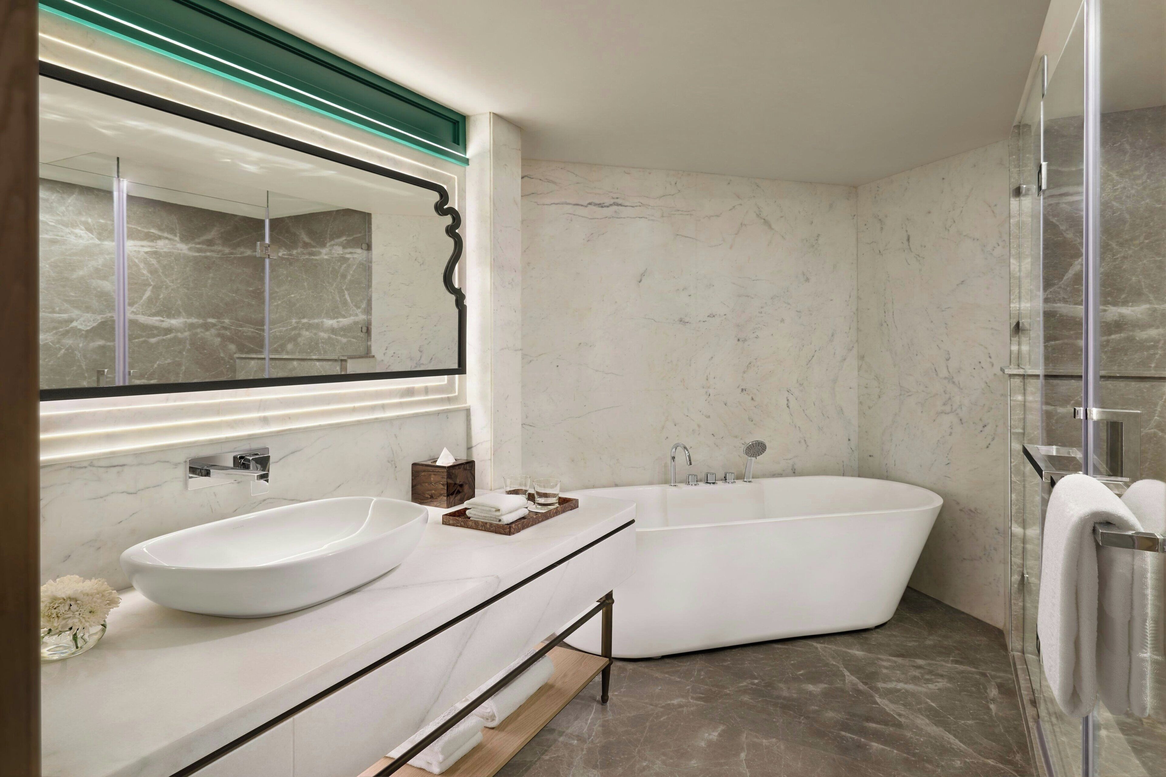 Un baño moderno con una bañera independiente, un espejo grande y un lavabo blanco.