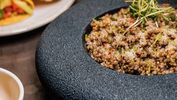 A stone bowl filled with quinoa salad, a plate of tacos, and a small bowl of spices on a dark surface.
