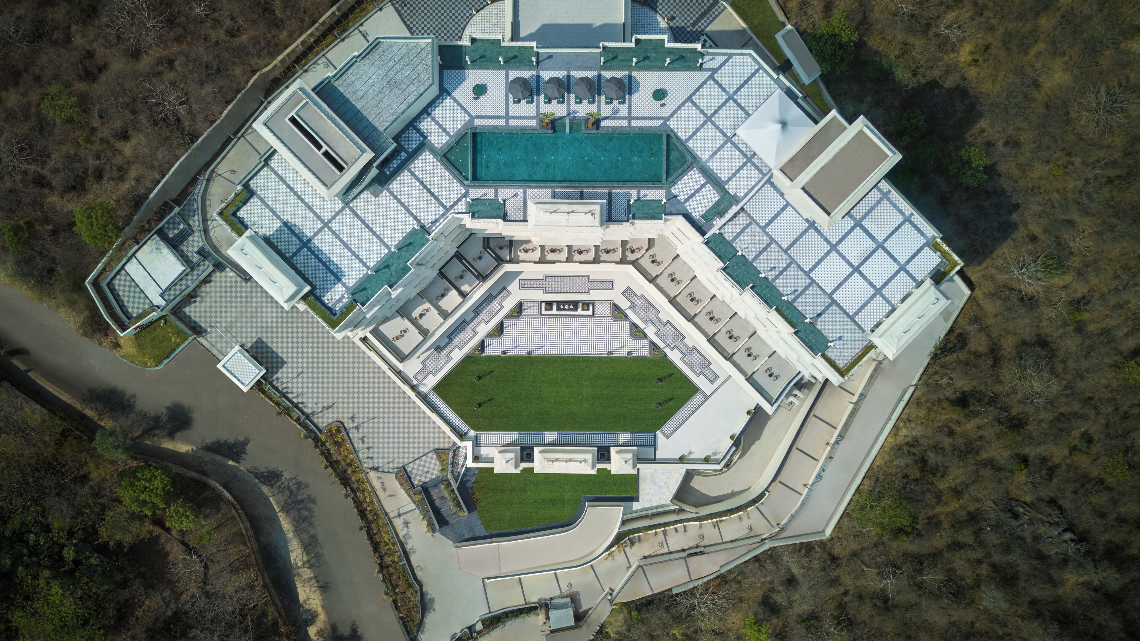Vue aérienne d’un hôtel moderne doté d’une cour intérieure, de plusieurs piscines et d’un motif à carreaux sur le sol de la cour.