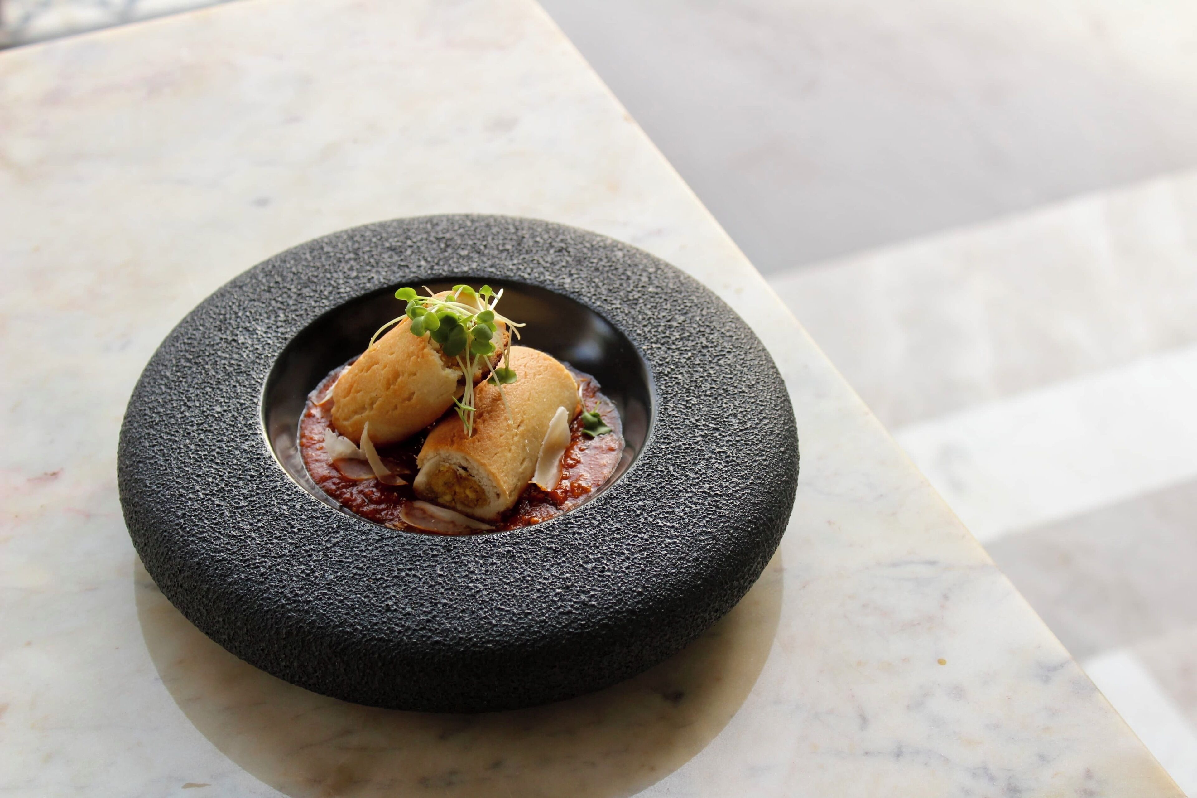 A dish with a black bowl on a marble surface.