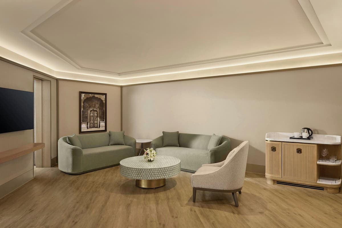 Un salon moderne avec un canapé d’angle vert, une table basse ronde, un fauteuil beige et un meuble en bois surmonté d’un plan de travail en marbre.