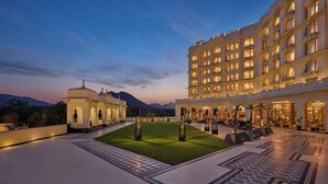 Pátio de hotel com gramado central, piso estampado e um edifício grande com várias sacadas.