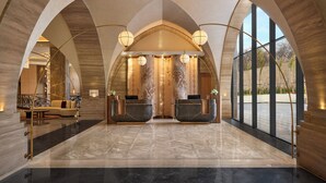 Um lobby espaçoso com teto alto e design em arco, com balcão de recepção, área de estar e grandes janelas que oferecem vistas.