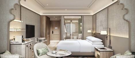 A modern hotel room with a large bed, a sitting area with a round table, a TV, and a bathroom visible through a glass door.