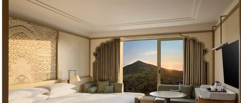 A hotel room with a large bed, a sofa, a small table, and a view of a mountainous landscape.