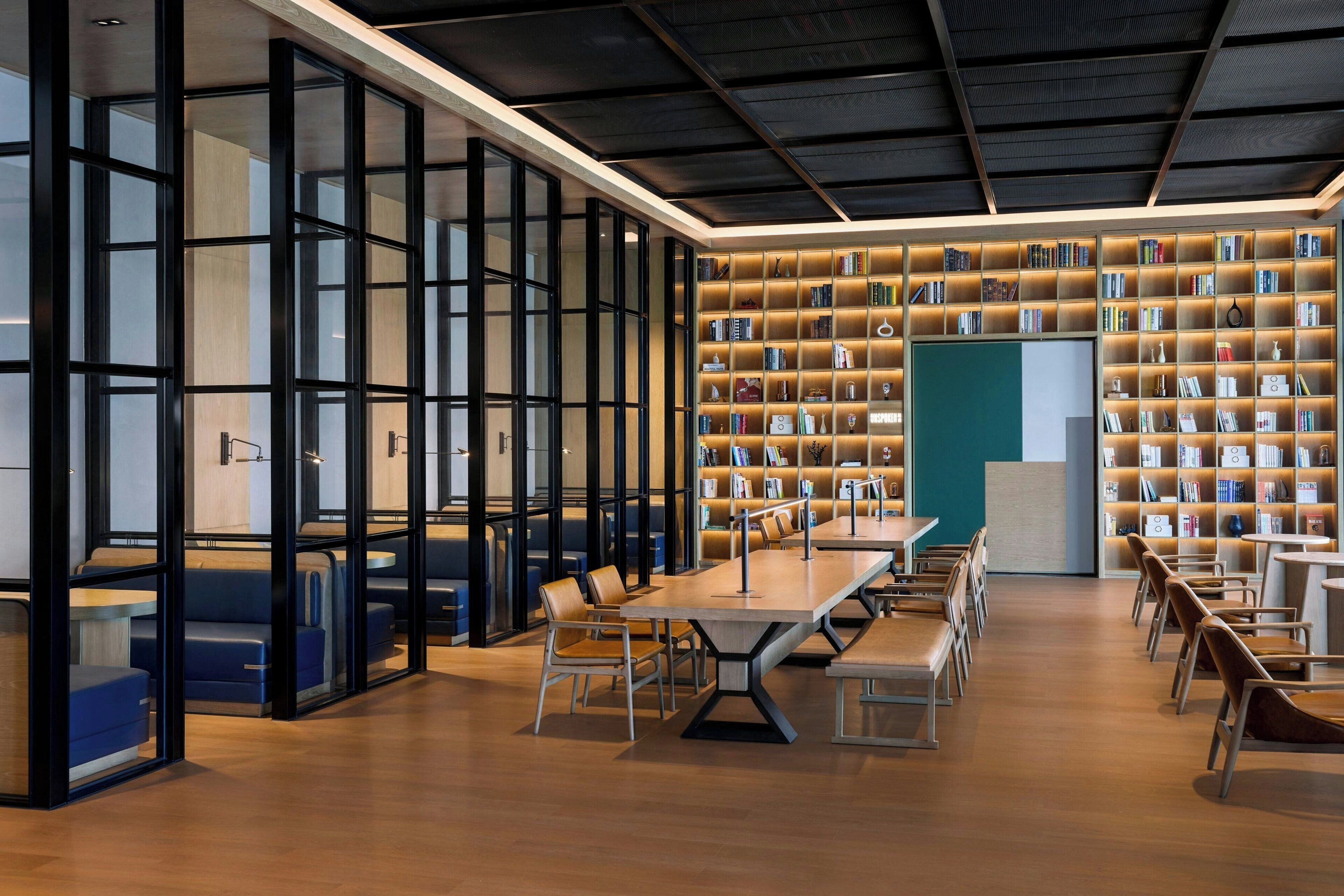 A modern library with bookshelves, seating areas, and a large table.