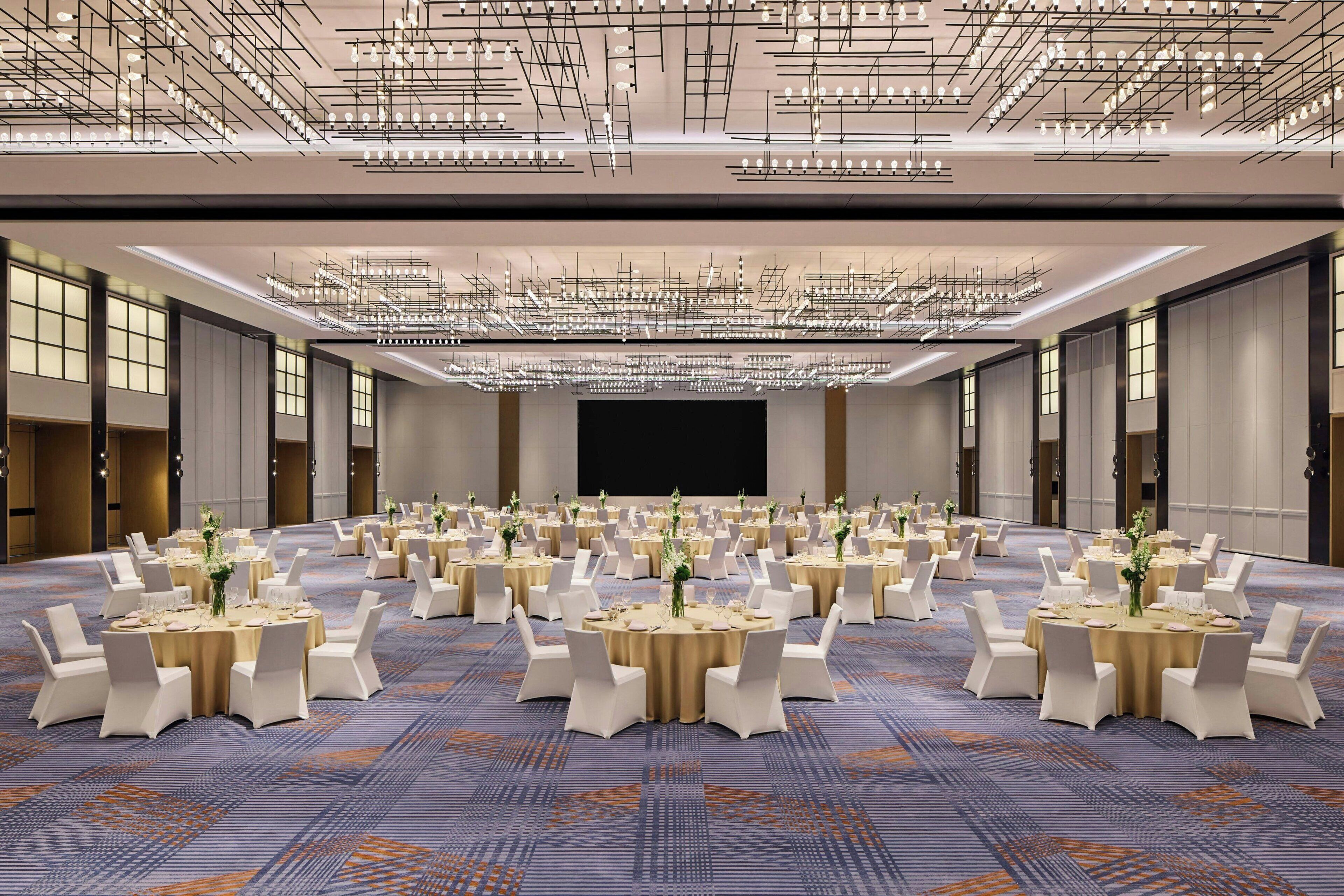 A large conference room with round tables, white chairs, and a modern chandelier.