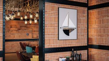 Un mur de briques orné d’un tableau représentant un voilier encadré, une table en bois avec des bouteilles et un luminaire suspendu.