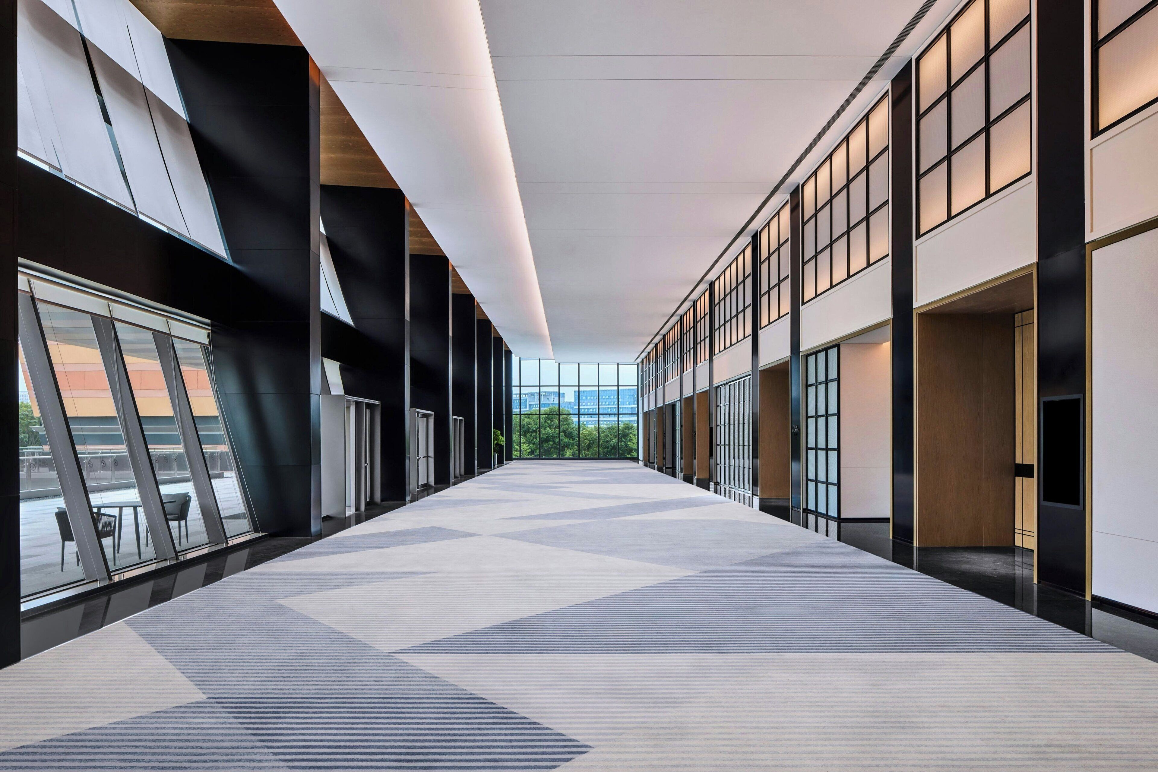 A modern interior with a long corridor, large windows, and a geometric patterned floor.