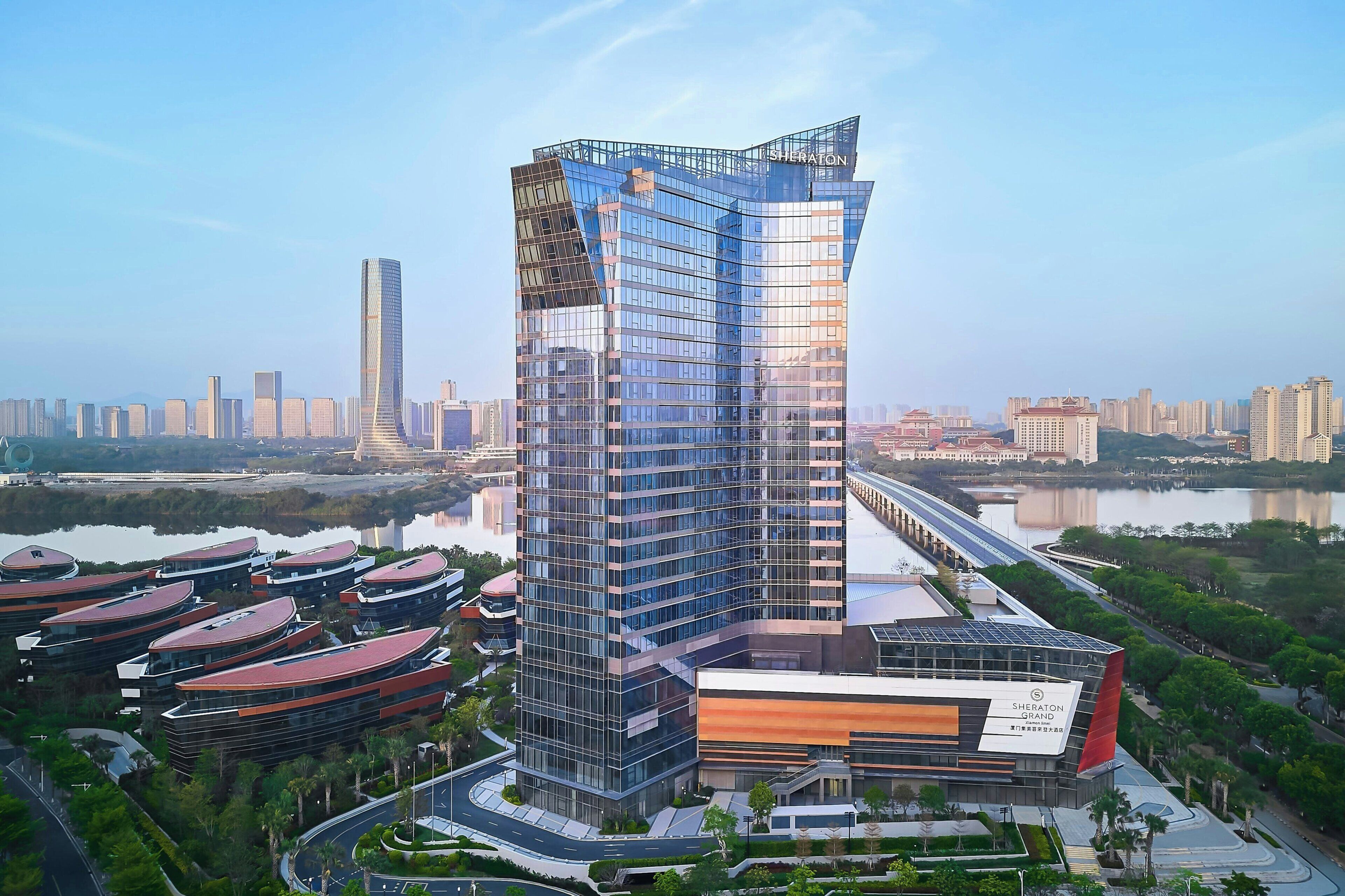 A modern high-rise building with a unique angular design, surrounded by a landscaped area with curved roads and smaller buildings.