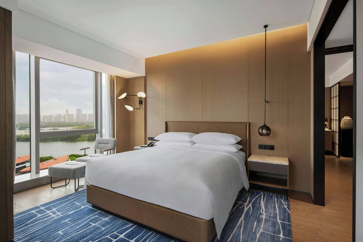 Ein modernes Hotelzimmer mit einem großen Bett, Blick auf eine Stadtlandschaft und einem Balkon mit Flussblick.
