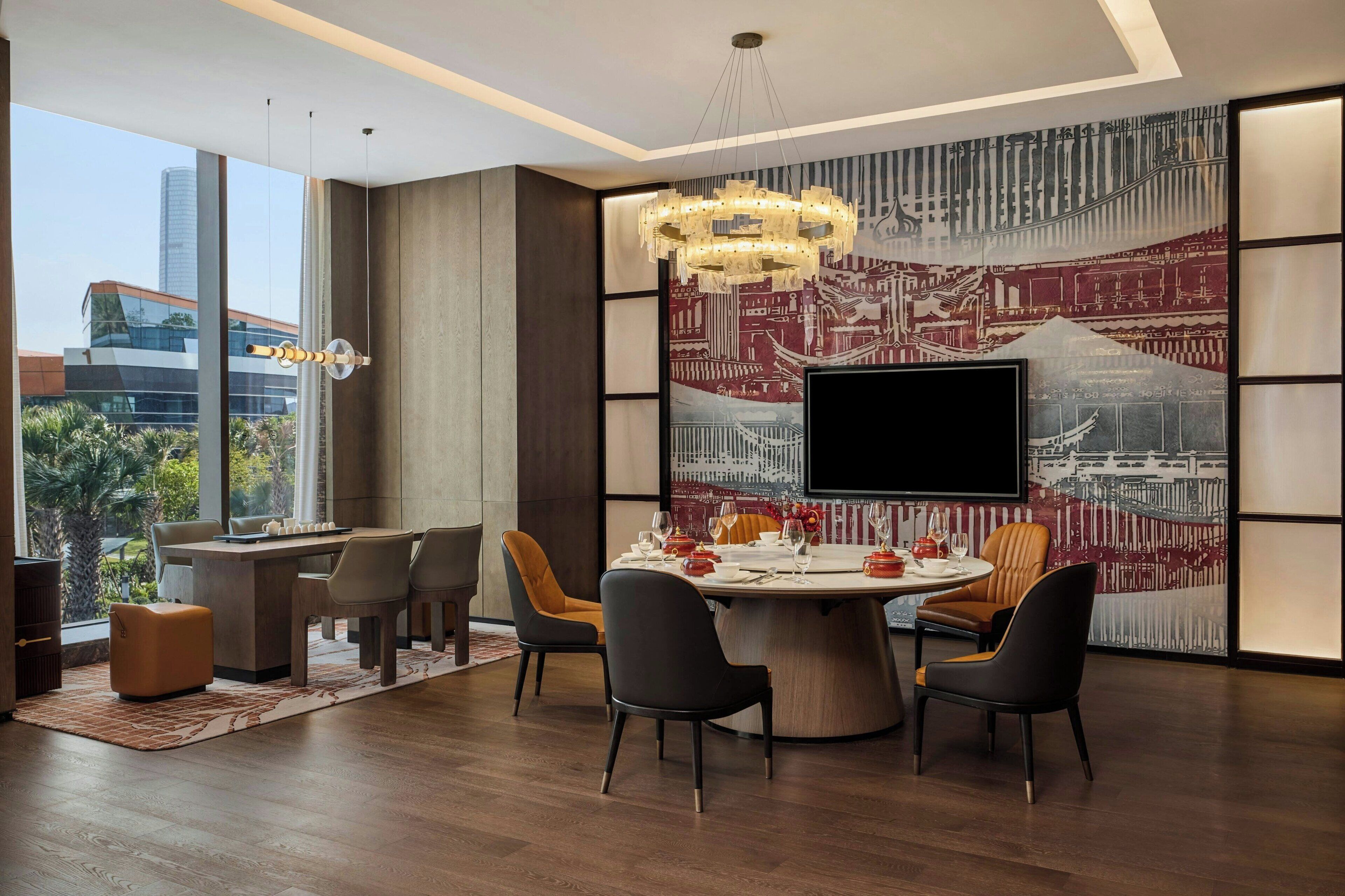 A modern dining area with a round table, chairs, and a large flat-screen TV.