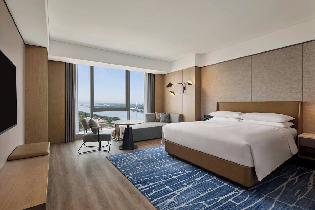Ein modernes Hotelzimmer mit einem großen Bett, einer Sitzecke mit Blick und einem Flachbildfernseher.
