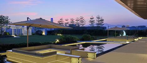 A modern outdoor area with seating, a pool, and umbrellas.
