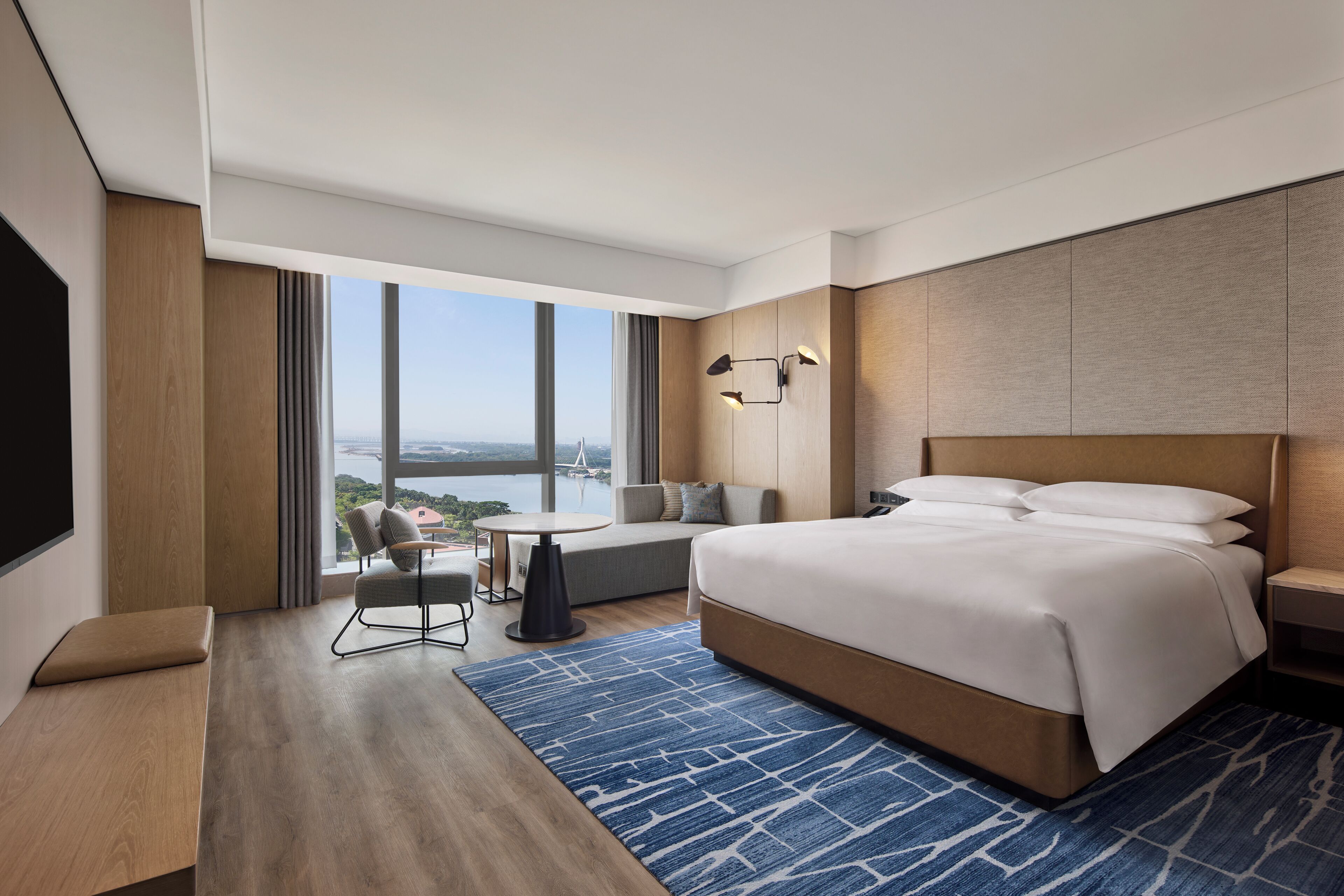 Une chambre d’hôtel moderne dotée d’un grand lit, d’un coin salon avec vue et d’une télévision à écran plat.