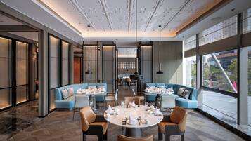 A modern dining area with round tables, blue sofas, and a view of the city through large windows.