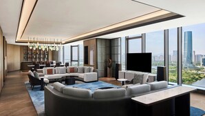 A modern living room with a large sectional sofa, a coffee table, and a TV. There is a city view through large windows. - Sheraton Grand Xiamen Jimei (Xiamen)